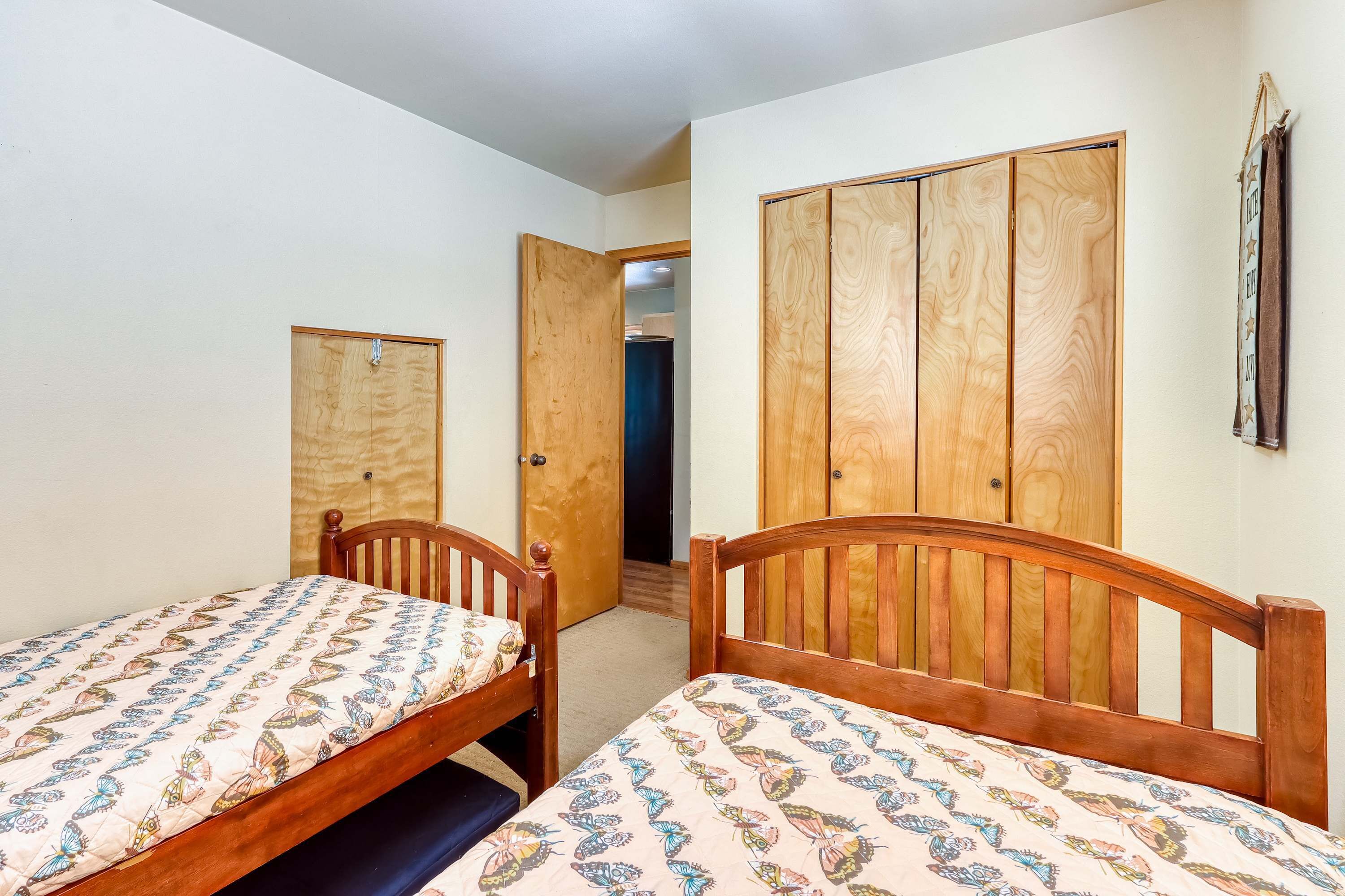 A room with two wooden beds, a wardrobe, and a door leading to another room.