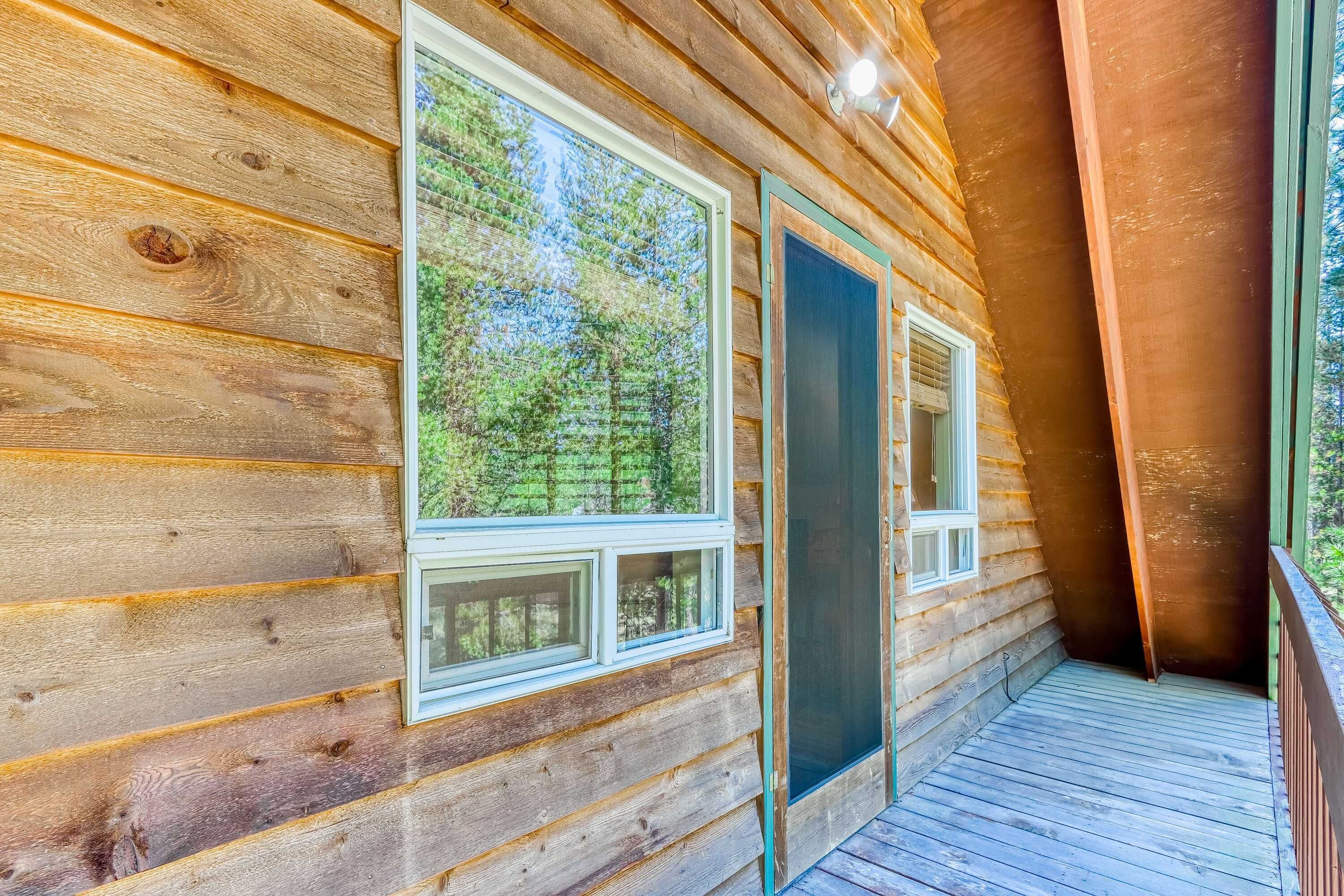 Una baita di legno con ampie finestre, un balcone e vista sulla foresta.