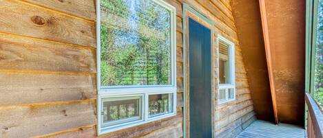 A wooden cabin with large windows, a balcony, and a view of the forest.
