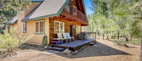 A log cabin with a deck, outdoor seating, and a dirt yard surrounded by trees.