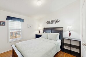 A bedroom with a bed, two bedside tables, a window with blinds, a decorative wall piece, and a door. - Dog-friendly single-level home with ramp entry access, firepit, W&D and WIFI (Bandon)