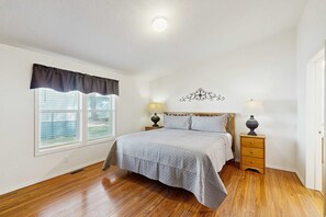 Une chambre à coucher comprenant un lit, deux tables de chevet avec des lampes, une fenêtre avec des stores et un élément décoratif mural.