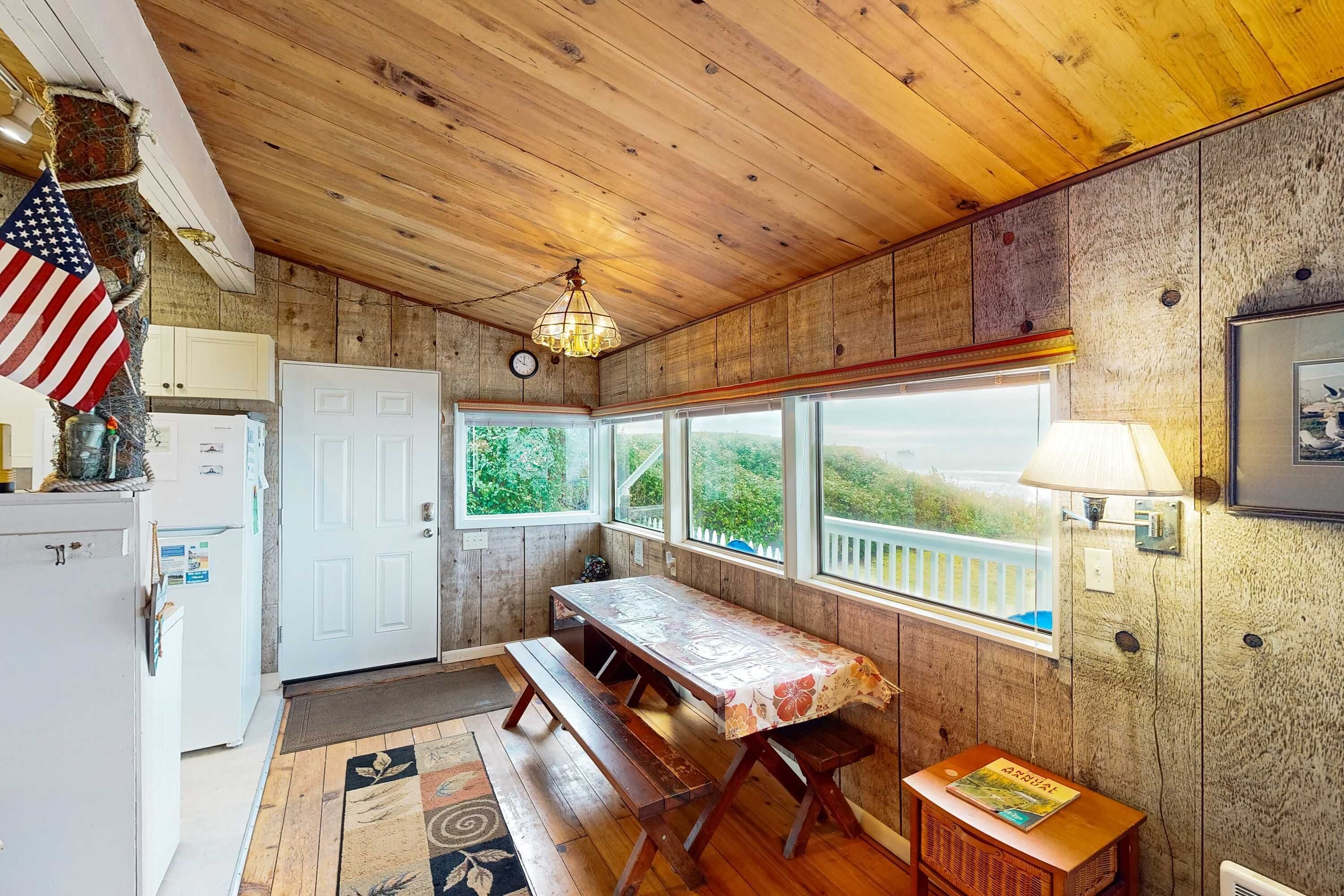 A wooden interior with a table, bench, and windows overlooking greenery.
