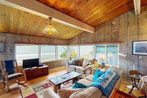 A cozy living room with a wooden ceiling, a television, a sofa, a coffee table, and a view of the outdoors. - Comfy oceanfront home three blocks to the beach with amazing views - dogs OK (Arch Cape)