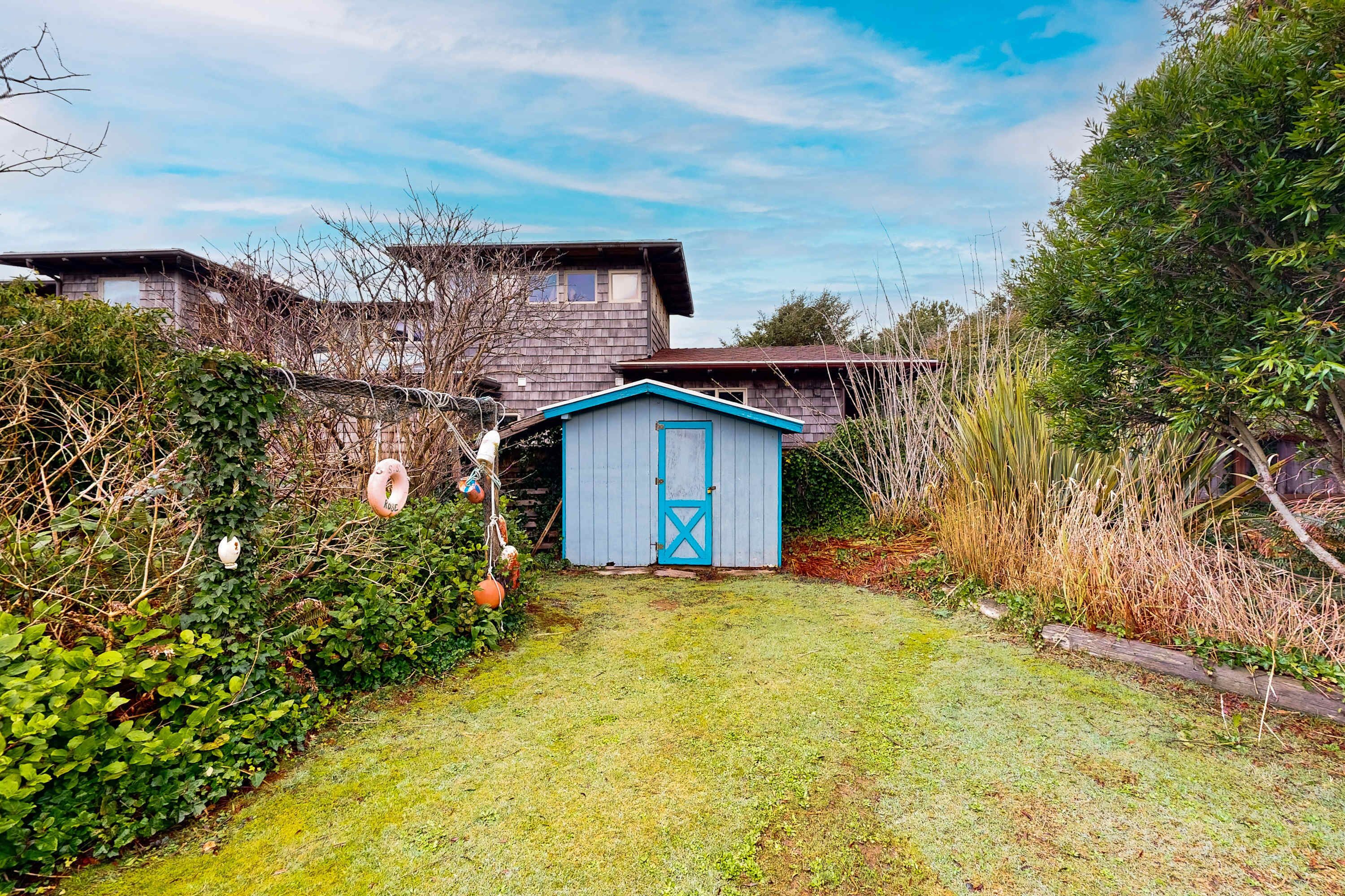 Une maison avec une porte de garage bleue, une cour couverte d’herbe et une clôture en bois.