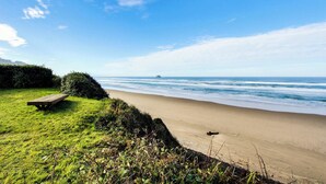 Une plage avec un banc en bois, une zone herbeuse et une vue sur l’océan.