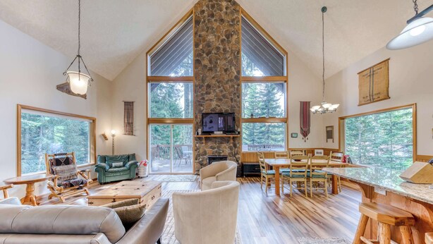 A spacious living area with a stone fireplace, large windows, and a dining area. - Mountain-view house near skiing with a great kitchen & private hot tub (Government Camp)