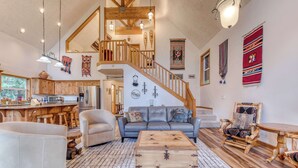 A spacious living area with a staircase, wooden furniture, and a kitchen in the background. - Mountain-view house near skiing with a great kitchen & private hot tub (Government Camp)