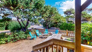 Une terrasse en bois, agrémentée de mobilier d’extérieur, entourée d’arbres et d’une clôture en bois.