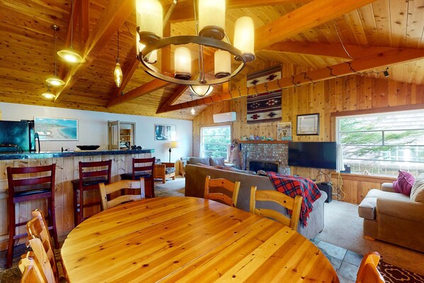 A wooden interior with a dining table, chairs, a sofa, a TV, and a fireplace.