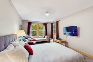 A hotel room with a bed, a desk, a chair, a lamp, a TV, and a window with curtains.