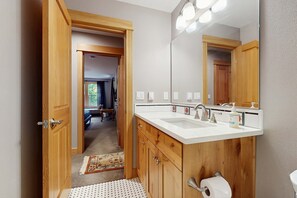 A bathroom with wooden cabinets, a white sink, a large mirror, and a toilet paper holder.