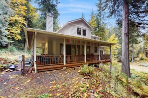 A two-story cabin with a covered porch, a chimney, and a gravel driveway.