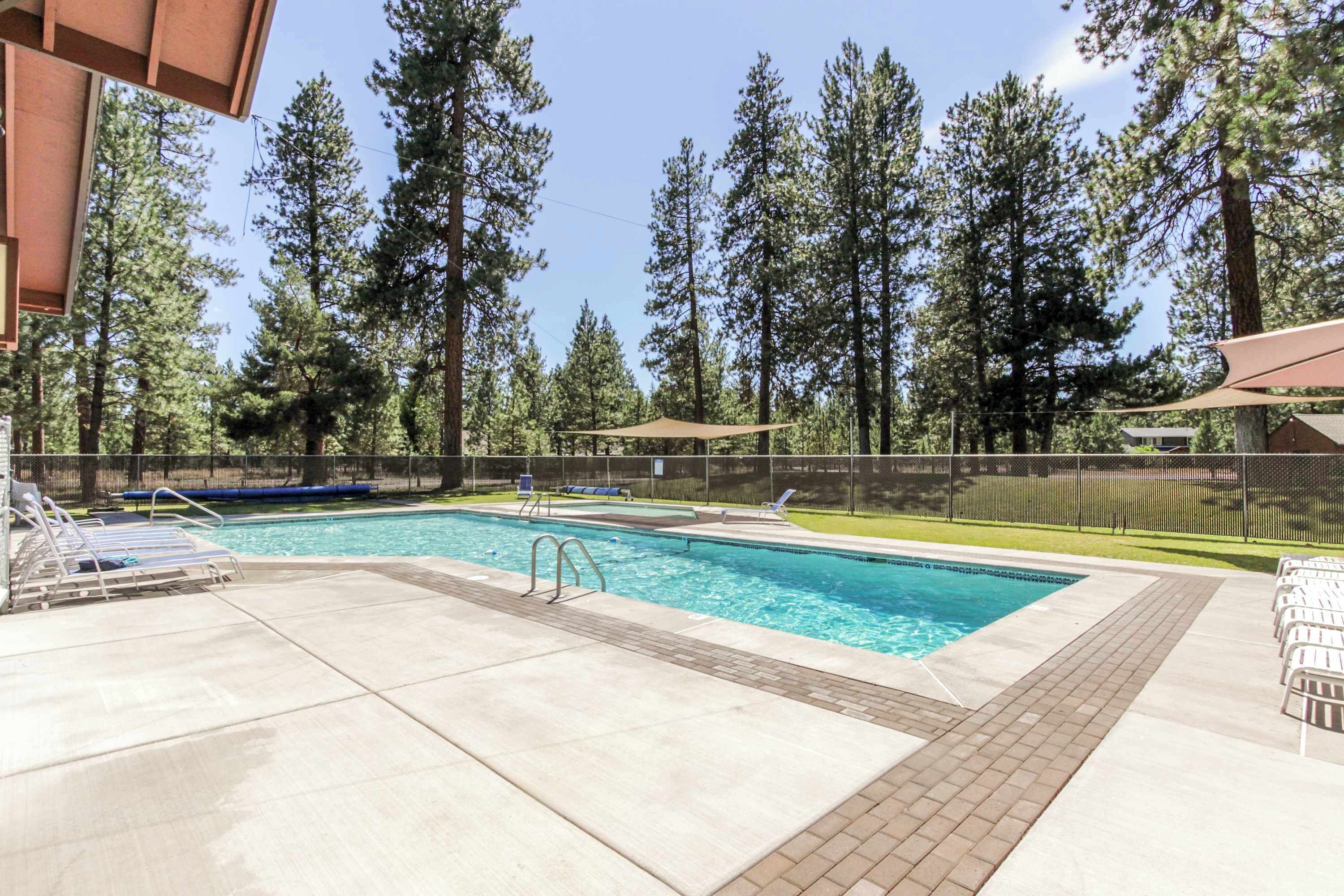 A swimming pool with lounge chairs, a shaded area, and a fenced yard with tall trees.