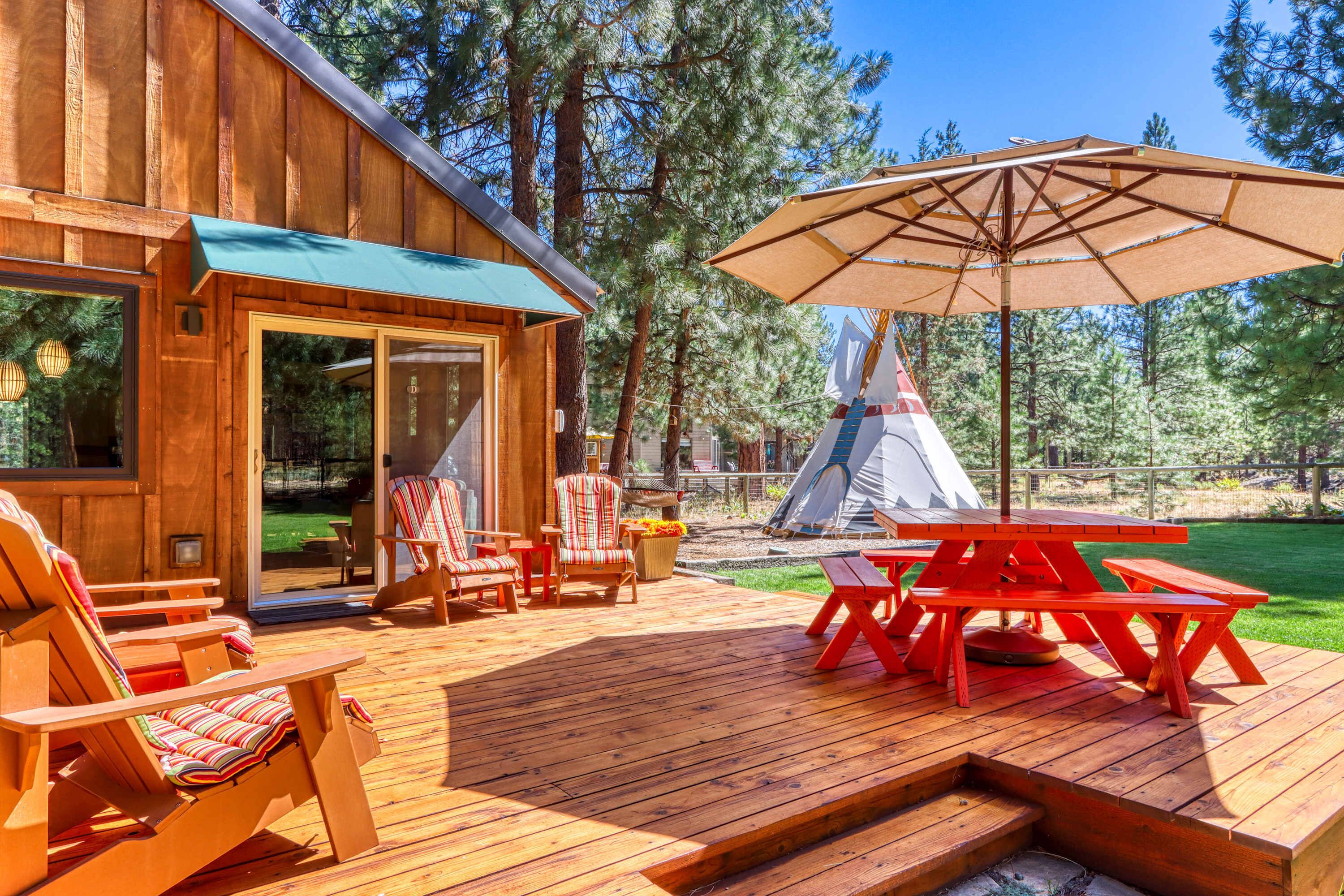 A wooden deck with outdoor seating and a picnic table, a tent in the background, and a clear view of the surrounding forest.