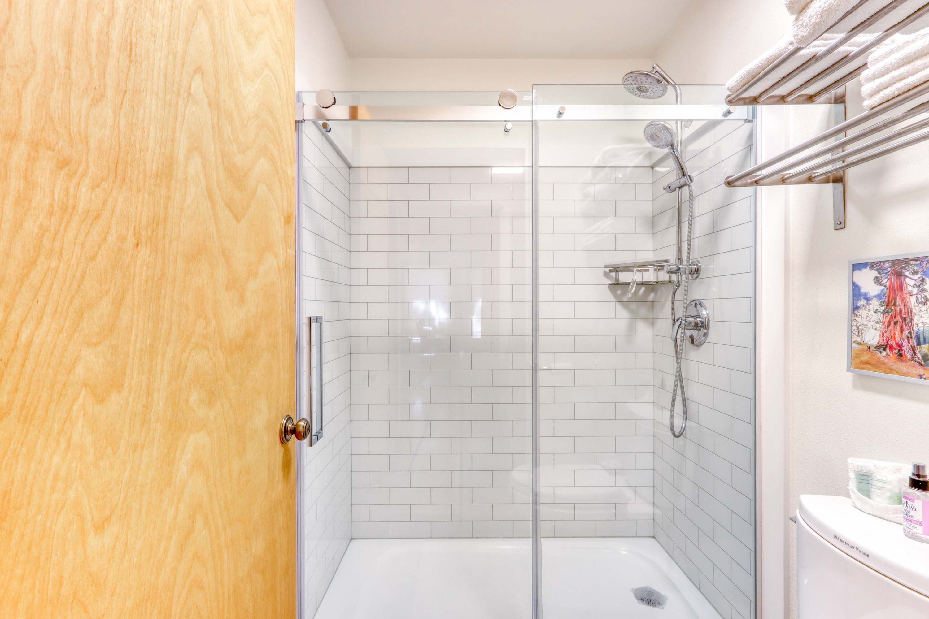 Eine Dusche mit Glastür, weiß geflieste Wände und eine weiße Badewanne.