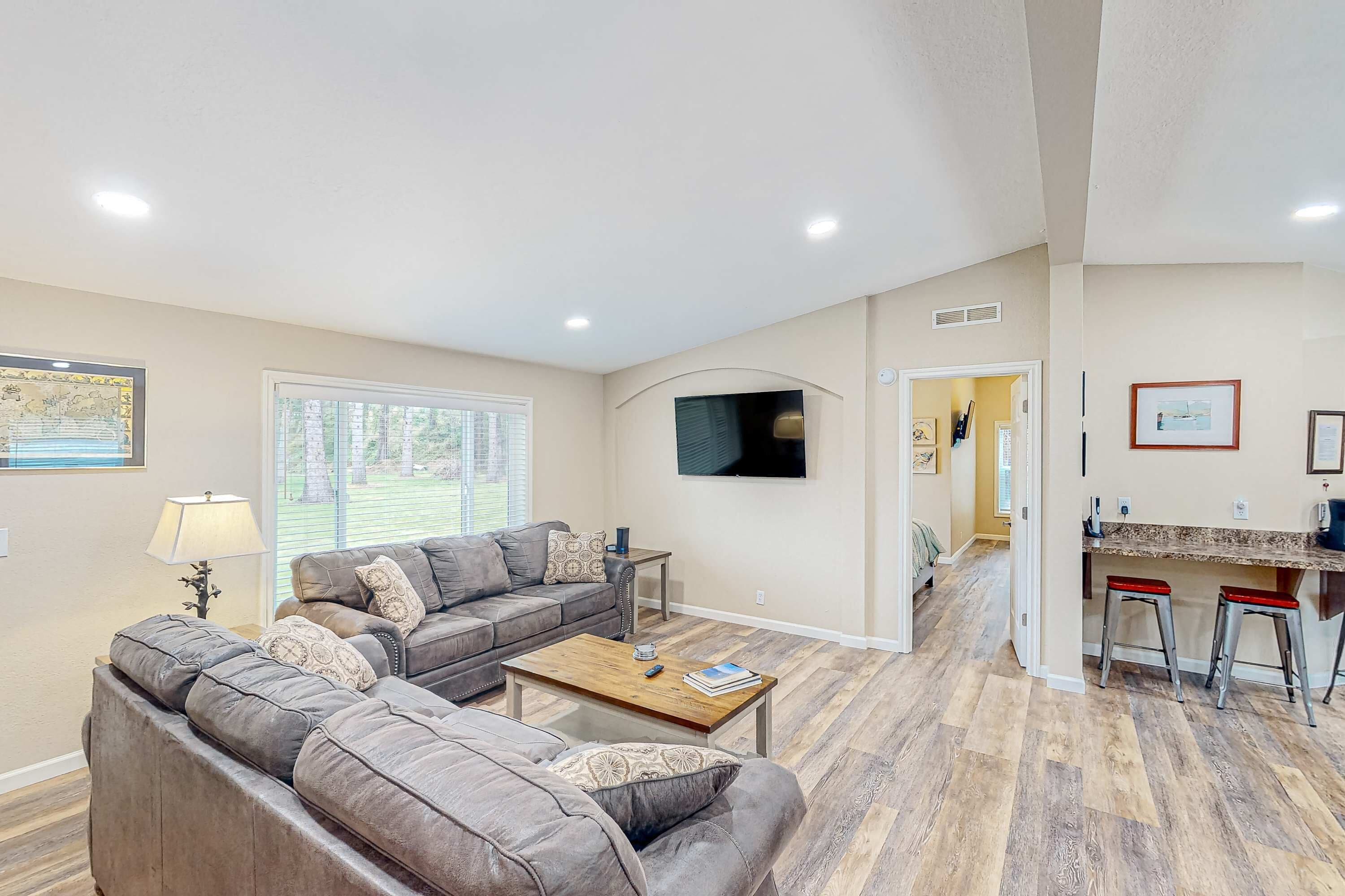 A living room with a sofa, coffee table, and TV, leading to a kitchen with stools.