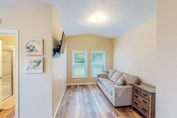 A living room with a beige sofa, a wooden cabinet, and two windows with blinds. - Modern, spacious home near the bay with grill, washer&dryer, & large yard (Coos Bay)