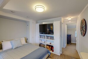 Une chambre à coucher comprenant un lit, un téléviseur, une bibliothèque et une porte donnant sur une autre pièce.