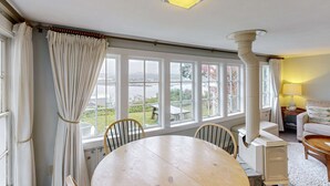 A room with a large window, a table, chairs, a sofa, and a heater.