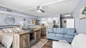 Een moderne woonkamer met een bank, een eettafel en een keuken met kasten en apparatuur.