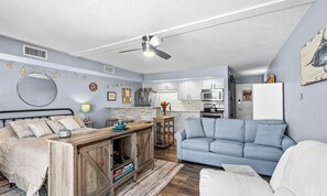Ein modernes Wohnzimmer mit einer Couch, einem Essbereich mit Tisch und einer Küche mit weißen Schränken und Geräten.