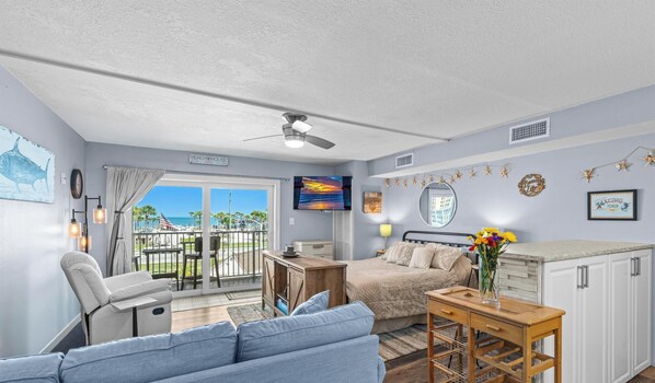 A room with a bed, a sofa, a small table, a TV, and a balcony with a view of the beach.