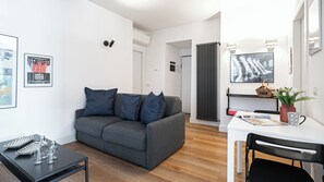A modern living room with a grey sofa, a small table with kitchenware, a white desk, and a chair. - Italianway Comfort - Baiamonti 3 A (Milan)