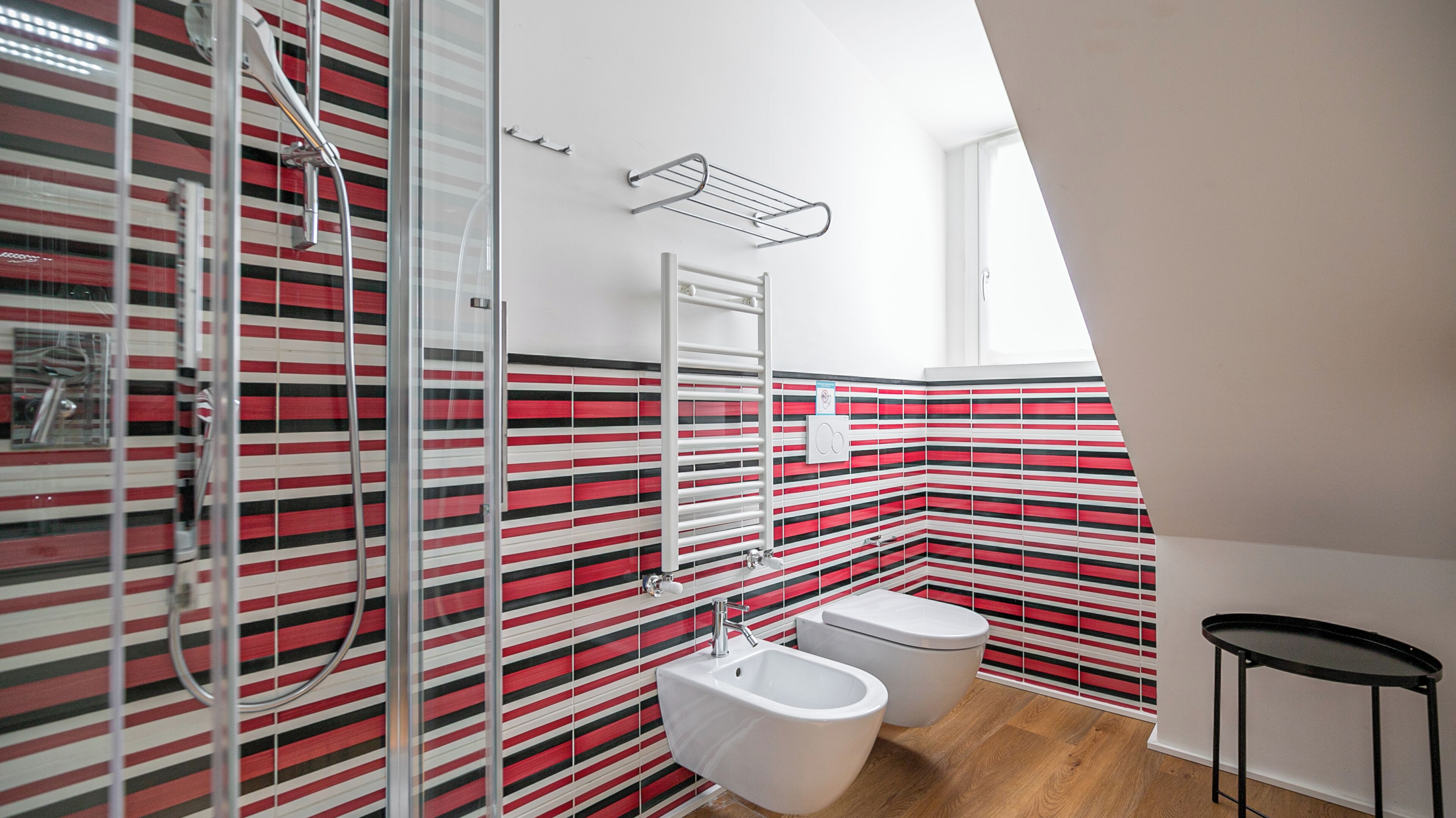Et moderne badeværelse med stribet flisebagningsvæg, bruser, toilet og et lille bord.