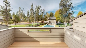 En balkon med udsigt over en swimmingpool, træer og omkringliggende huse.