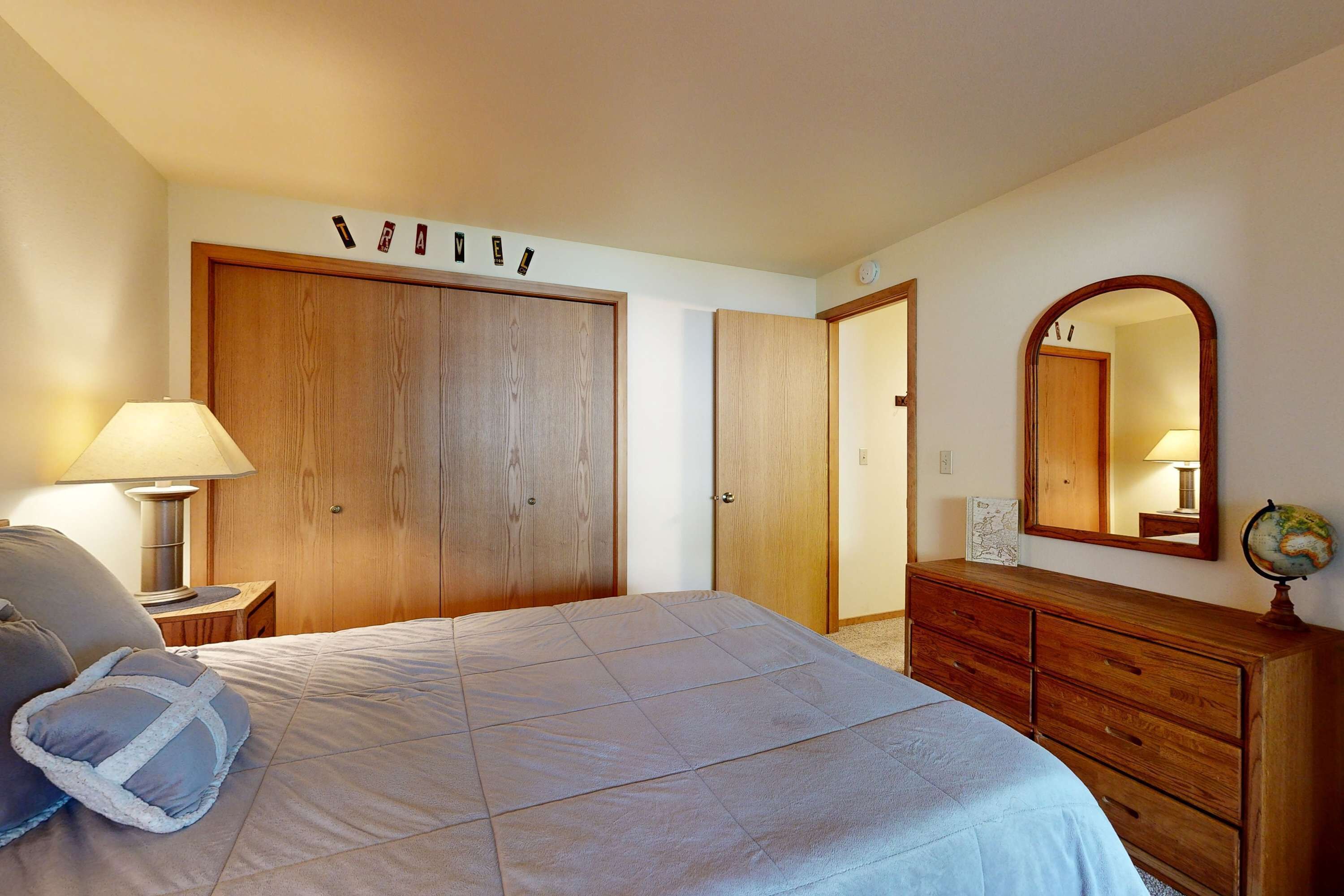 A bedroom with a bed, a dresser, a mirror, and a wall-mounted shelf with a globe.