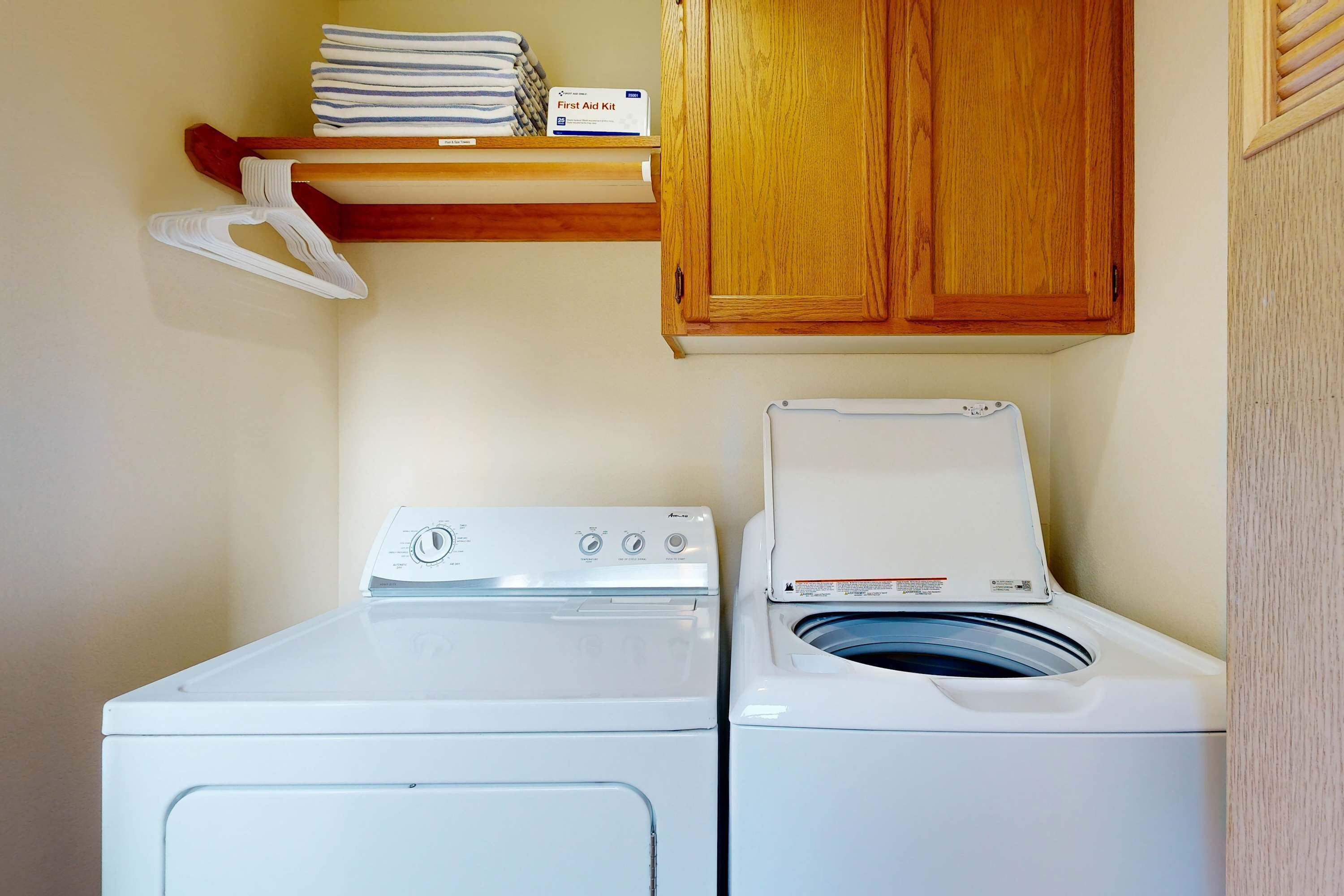 A laundry area with a front-loading washer and dryer, wooden cabinets, and a shelf with folded towels.