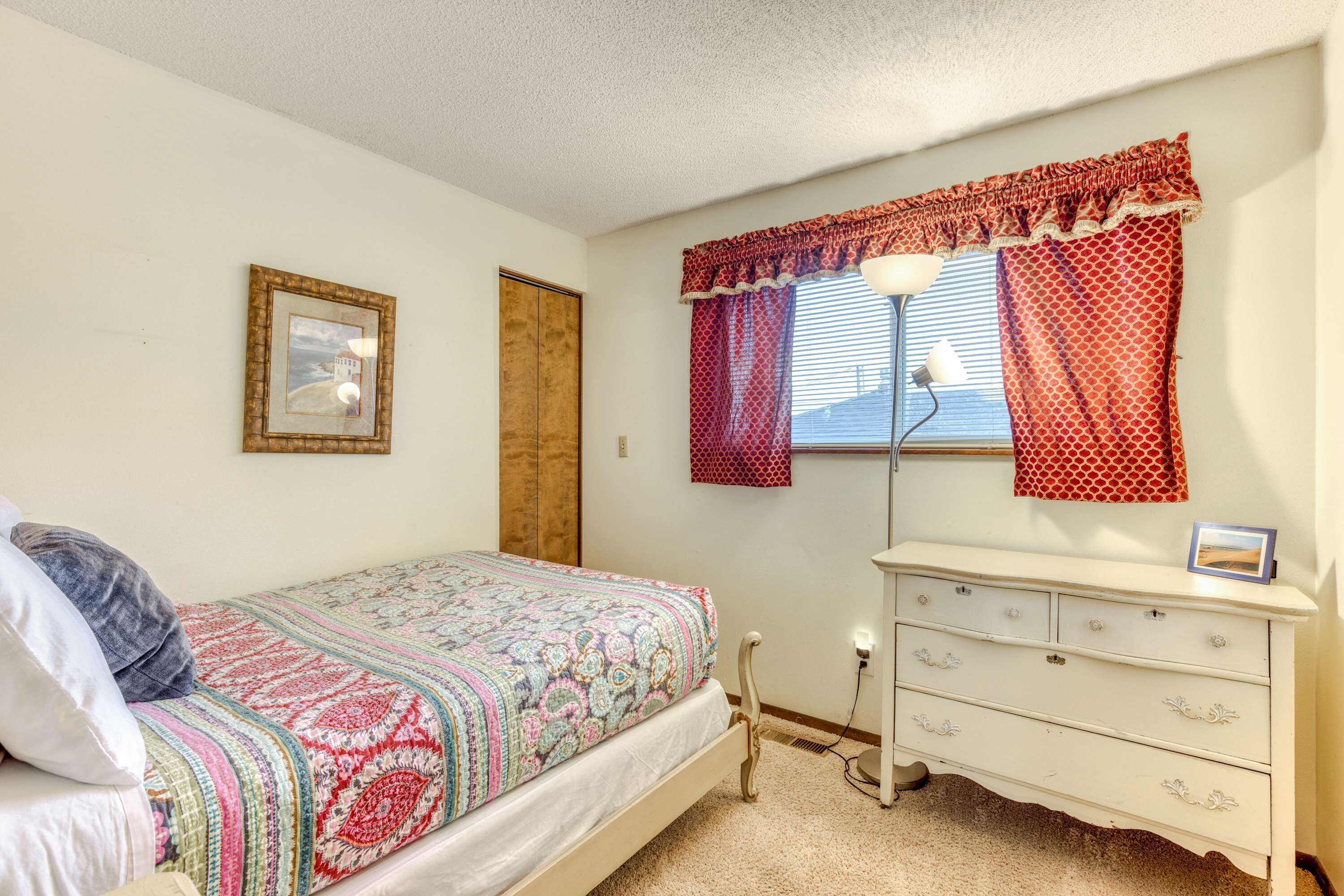 A bedroom with a bed, dresser, window with curtains, and a picture on the wall.