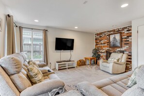 A living room with a sofa, a TV, a fireplace, and a window. - Spacious House with Entertainment Options & Very Close Beach Access (Seaside)