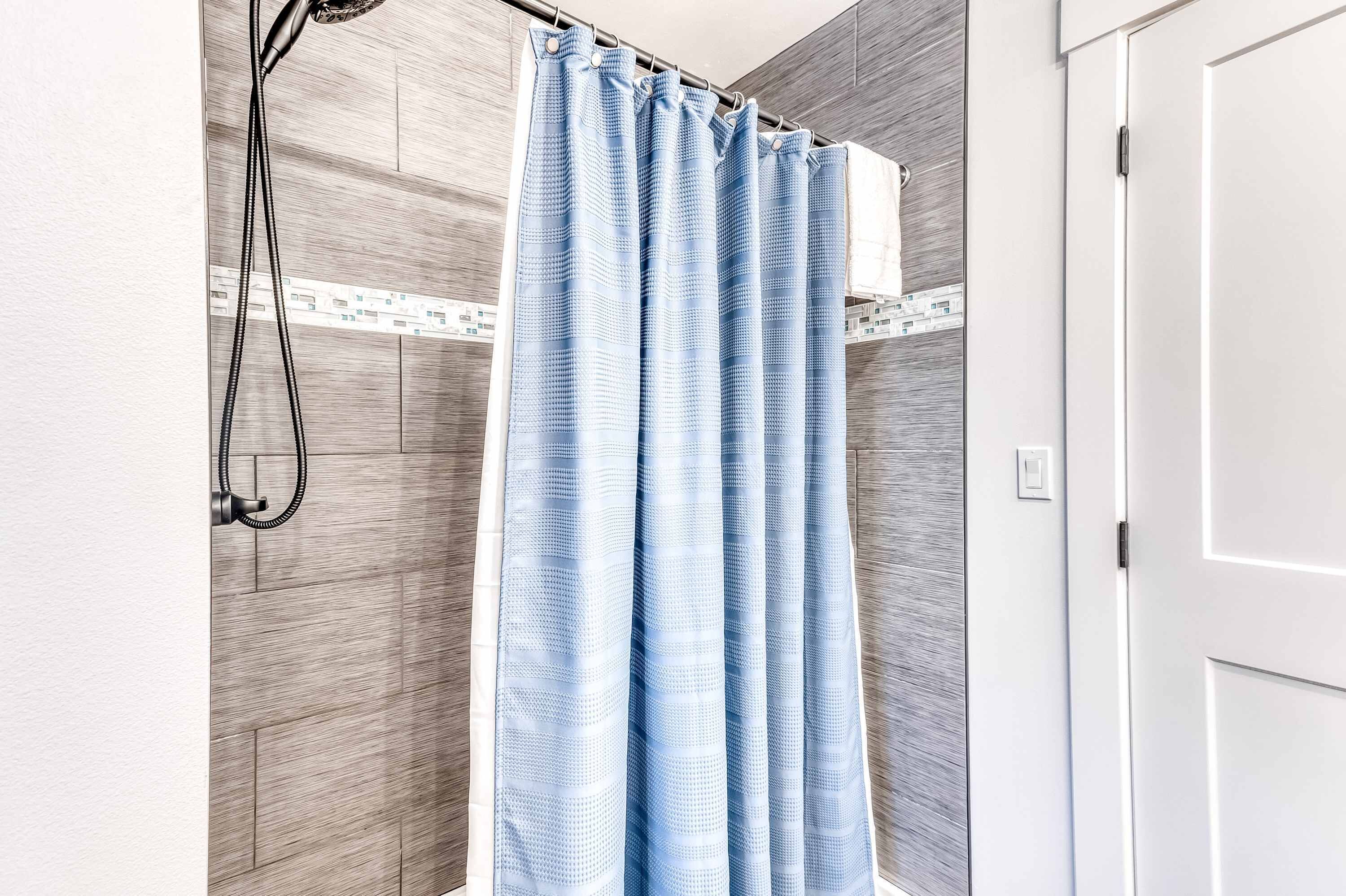 A shower area with a blue shower curtain, a handheld showerhead, and a tiled wall.