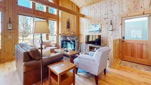 Een houten hutinterieur met een open haard, bank, fauteuil en televisie.