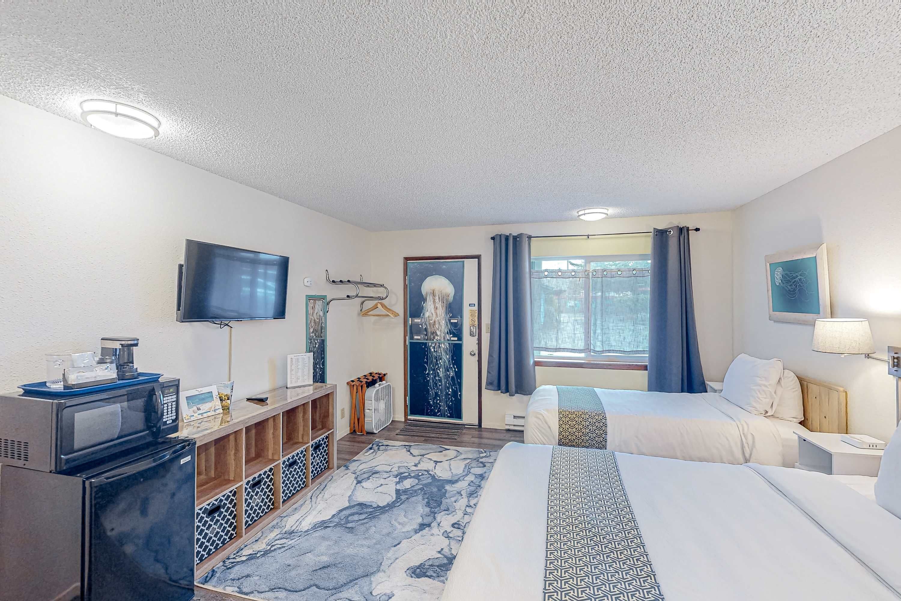 A hotel room with a bed, a TV, a desk, a microwave, and a refrigerator.