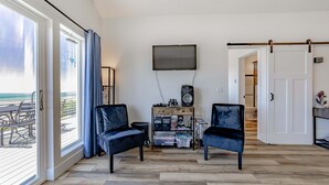 Une pièce dotée d’une porte coulissante donnant sur un balcon, d’un téléviseur fixé au mur, d’une petite table avec un haut-parleur et de deux chaises.