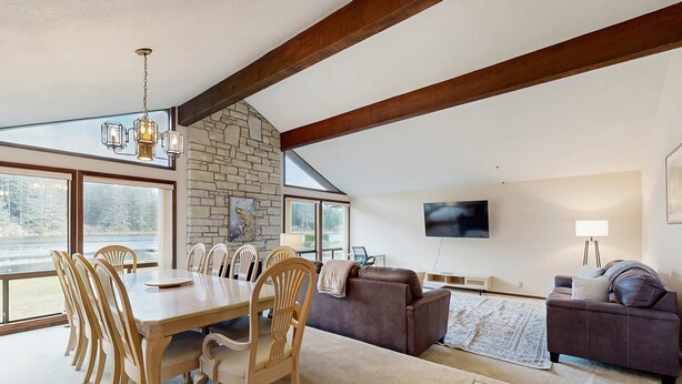 Un amplio salón con mesa de comedor, sillas, sofás, chimenea de piedra y ventanas grandes.