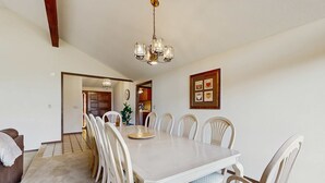 Un comedor con una mesa grande, sillas, una araña y un reloj en la pared.