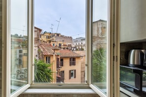 A view through a window of a building with multiple balconies, a tiled roof, and a mix of architectural styles. - iFlat | Stylish Crispi 20 Exclusive Apartment (Rome)