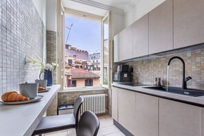A compact kitchen with a window view, a radiator, and a small dining area. - iFlat | Stylish Crispi 20 Exclusive Apartment (Rome)