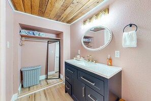 A bathroom with a wooden ceiling, a vanity with a mirror, a towel rack, and a laundry basket. - Dog-friendly rustic house near ocean and golf with washer/dryer & gas grill (Florence)