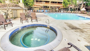 Uma banheira de hidromassagem cercada por espreguiçadeiras, uma piscina e um edifício com varandas.