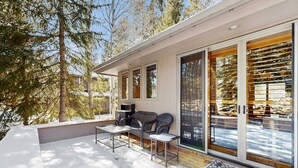 A covered outdoor area with a seating arrangement, a television, and a large sliding glass door. - Spacious Family Home with Hot Tub, AC, Garage Gym & SHARC Amenities (Sunriver)
