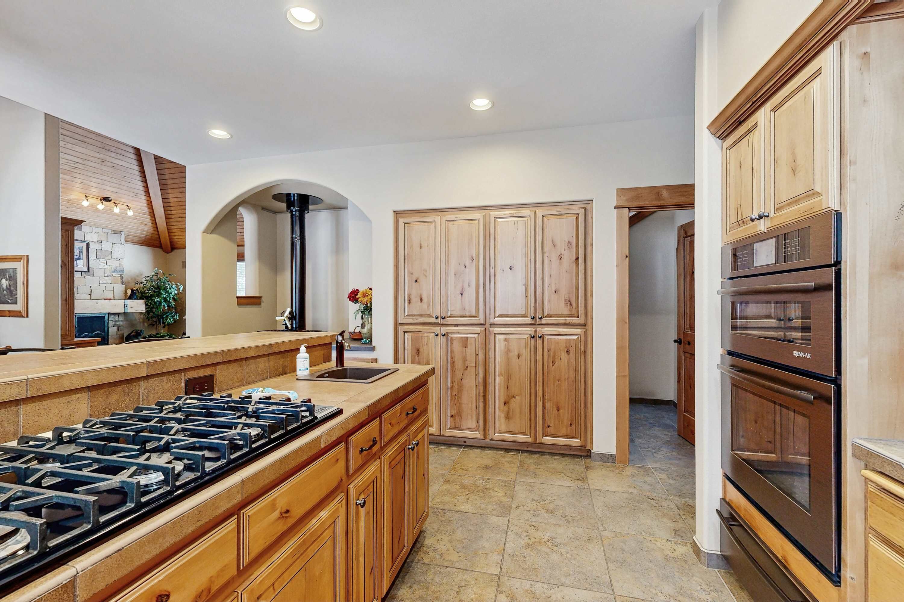 A kitchen with a central island, wooden cabinets, a built-in oven, and a stone tile floor.