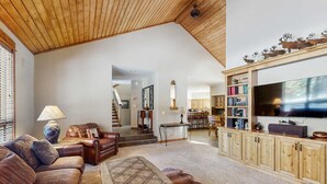 A spacious living room with a high ceiling, a fireplace, a television, and a dining area. - Spacious Family Home with Hot Tub, AC, Garage Gym & SHARC Amenities (Sunriver)