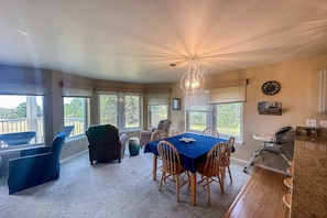 A dining area with a table and chairs, a chandelier, and large windows with blinds.
