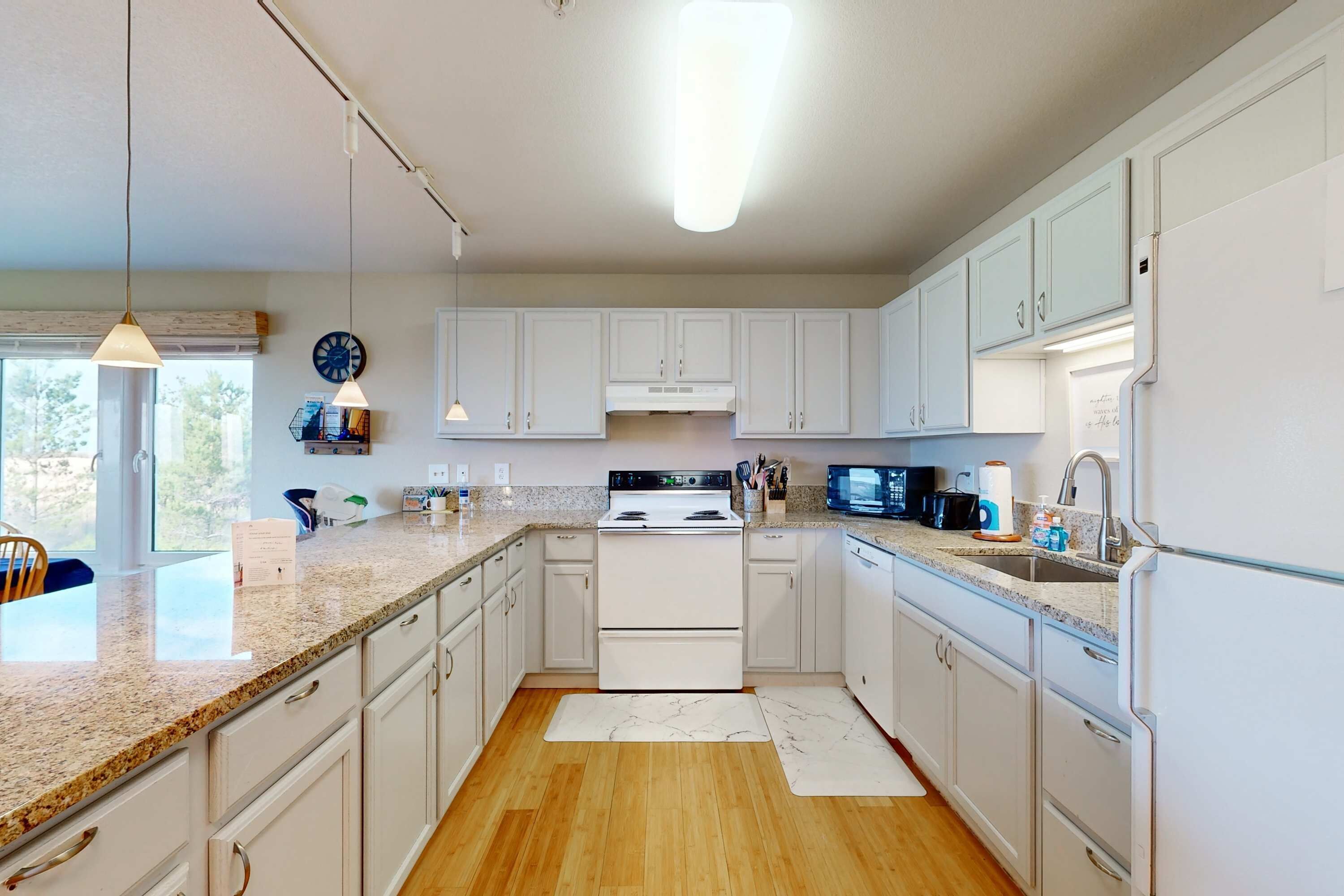 A kitchen with white cabinets, a stove, a microwave, and a sink.