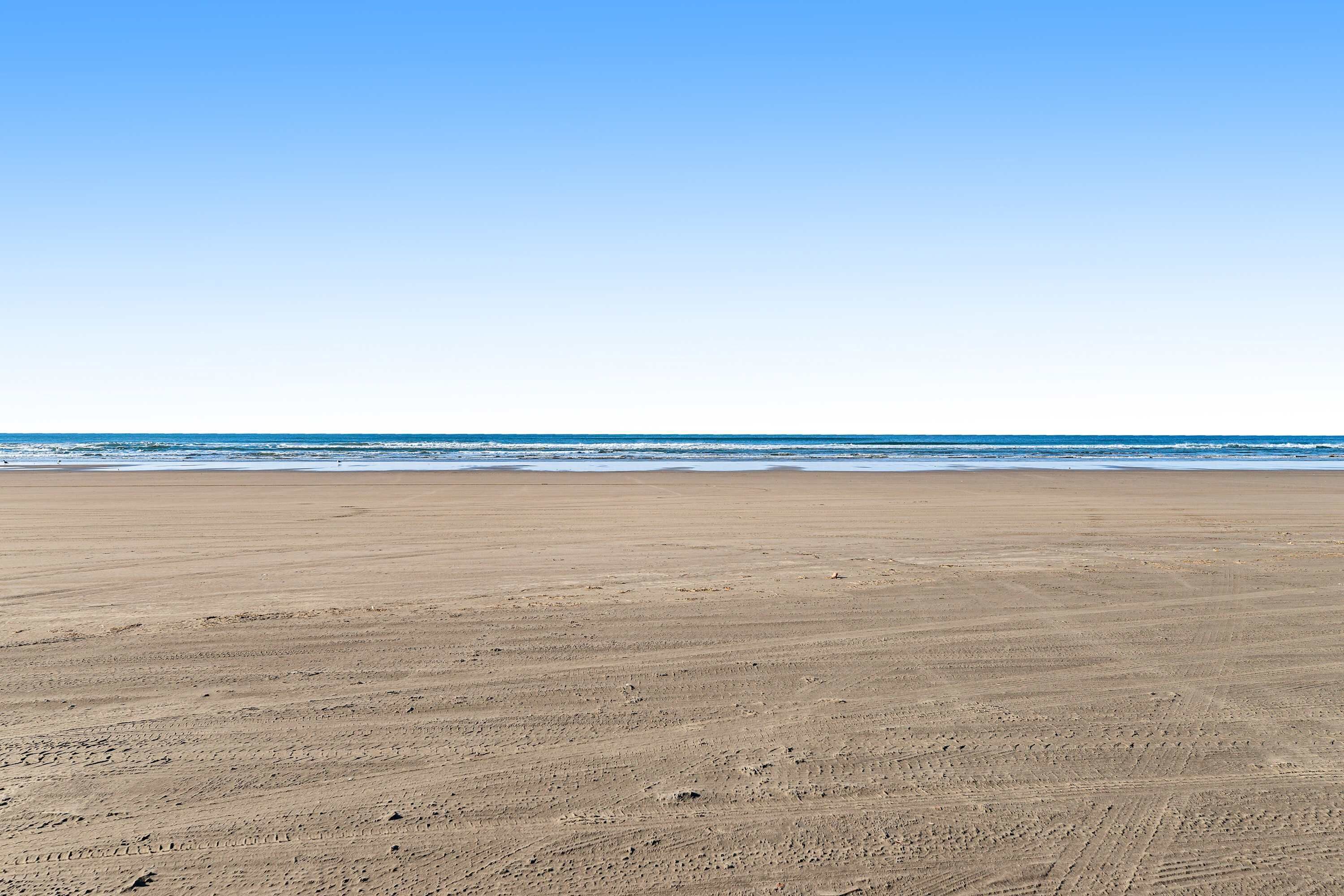 A wide sandy beach with gentle waves, clear sky, and no visible structures or people.